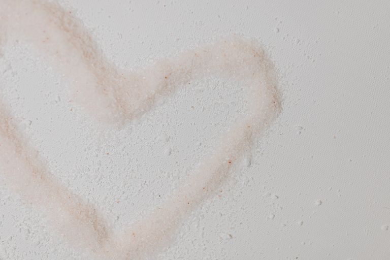 Pink Himalayan salt forming a heart shape on textured white surface, symbolizing love and self-care.