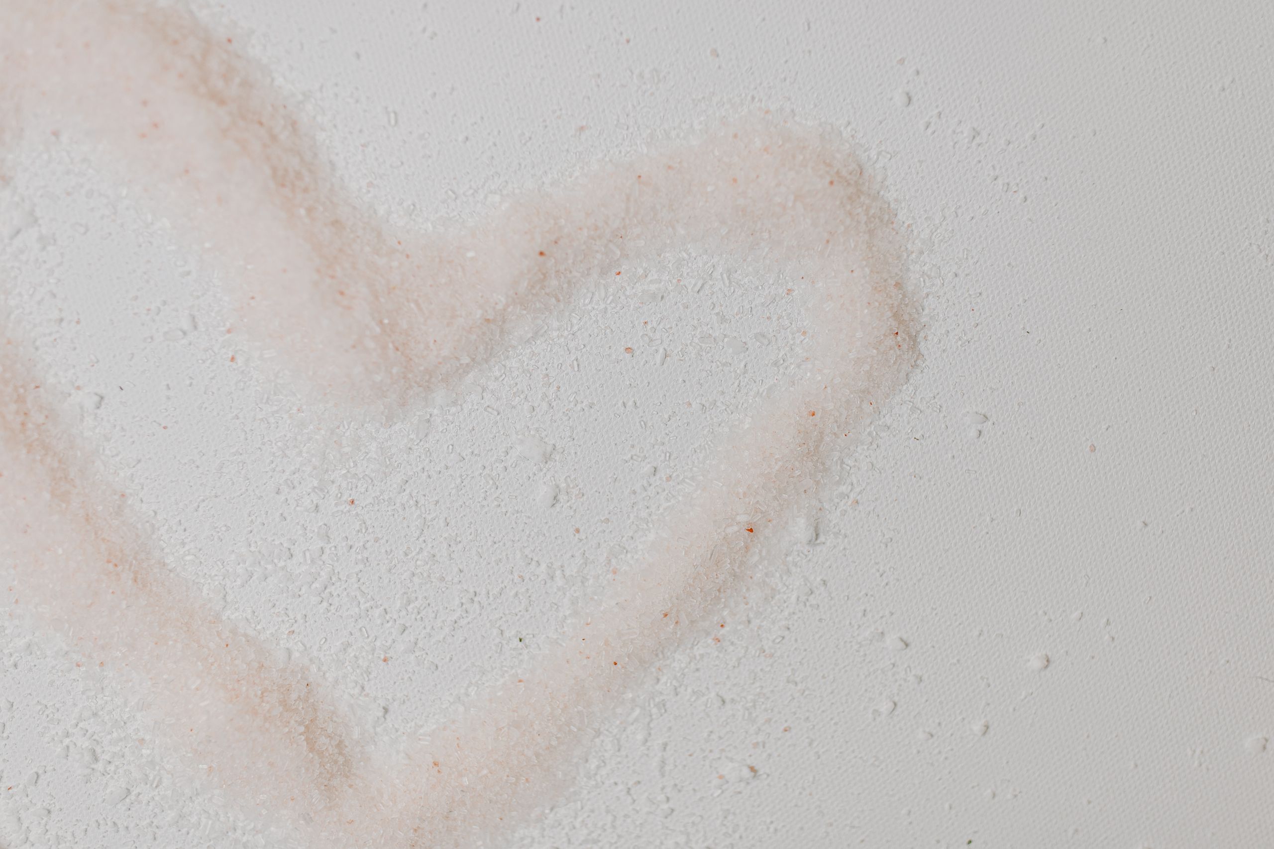 Pink Himalayan salt forming a heart shape on textured white surface, symbolizing love and self-care.